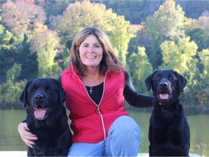 Smiling Loretta Cleveland, owner and trainer of The Positive Pooch, with two black labs by her sides